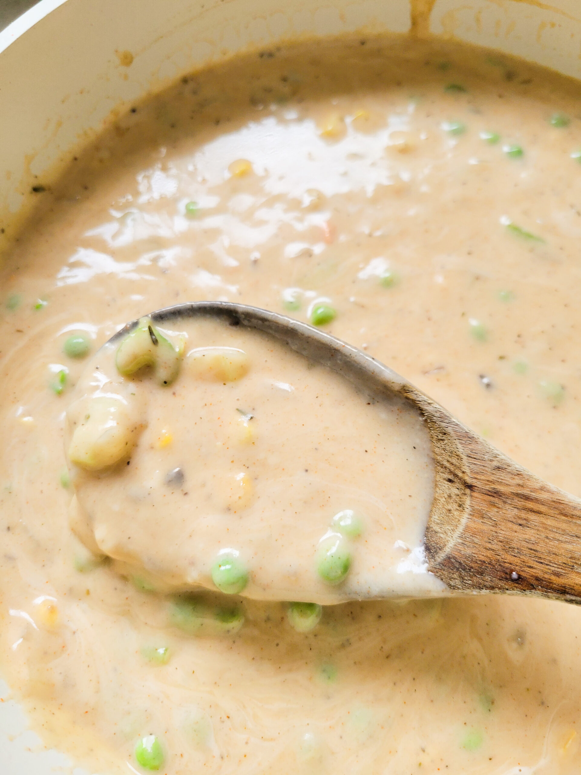 Creamy chicken pot pie filling with a wooden spoon stirring it. 